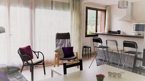 Ett kompakt bostadsutrymme med ett matbord, stolar, en soffa, ett köksområde med en spis och ett fönster med gardiner.