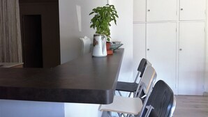 Ett modernt kök med en mörk bänkskiva, en krukväxt och ett vitt skåp.
