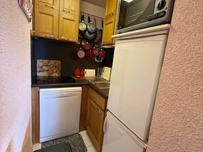 A compact kitchen with wooden cabinets, a microwave, a dishwasher, and a refrigerator.