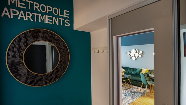A modern interior with a teal accent wall, a circular mirror, and a sign reading "METROPOLLE APARTMENTS".