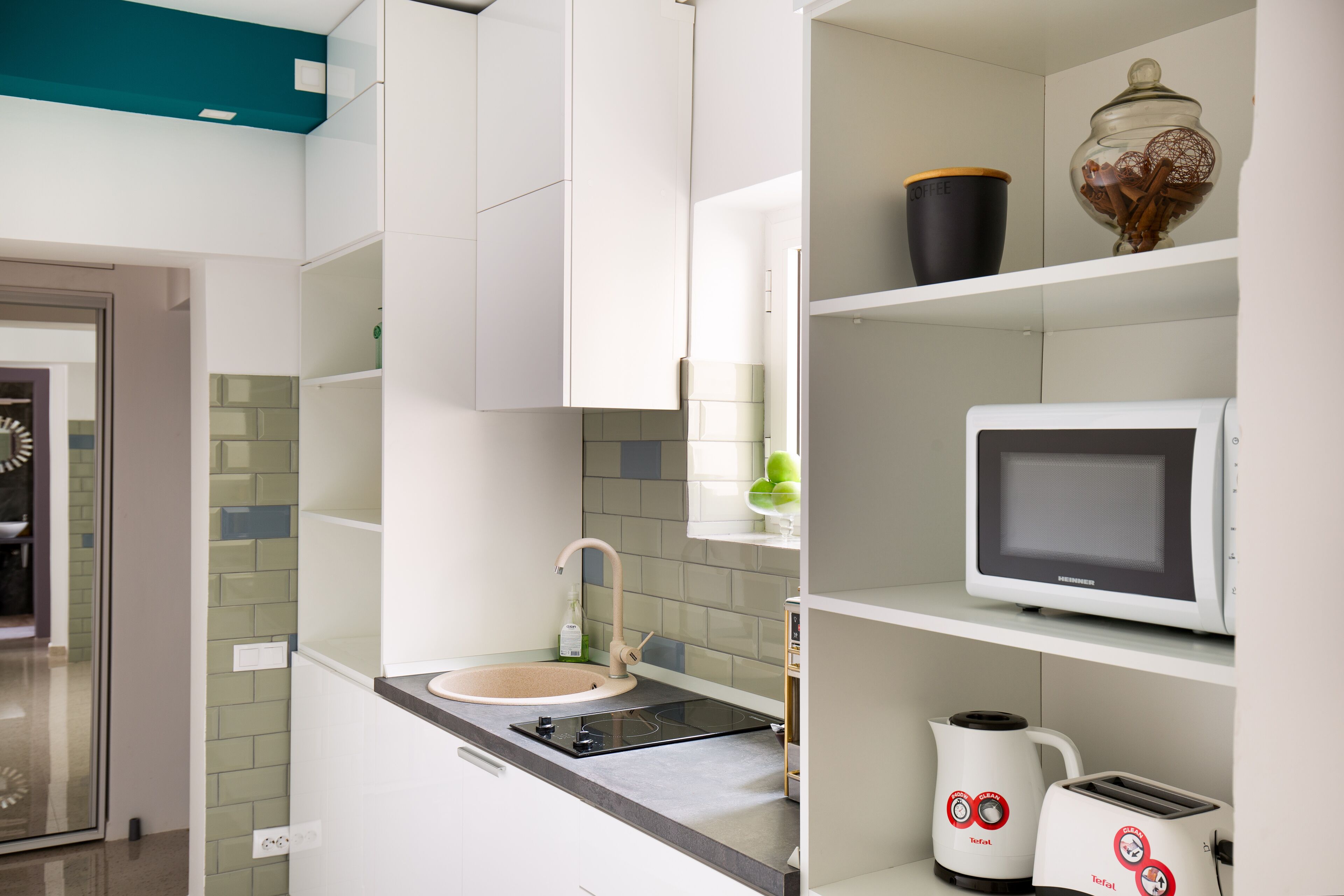 A modern kitchen with white cabinets, a sink, a stove, a microwave, and two coffee makers.