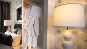 A hotel room with a bed, a mirror, a robe, and a lamp.