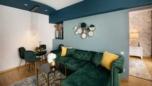 A modern living room with a green sectional sofa, a dining table with chairs, and a wall-mounted mirror.