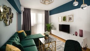 A modern living room with a green sofa, a flat-screen TV, and a minimalist design.
