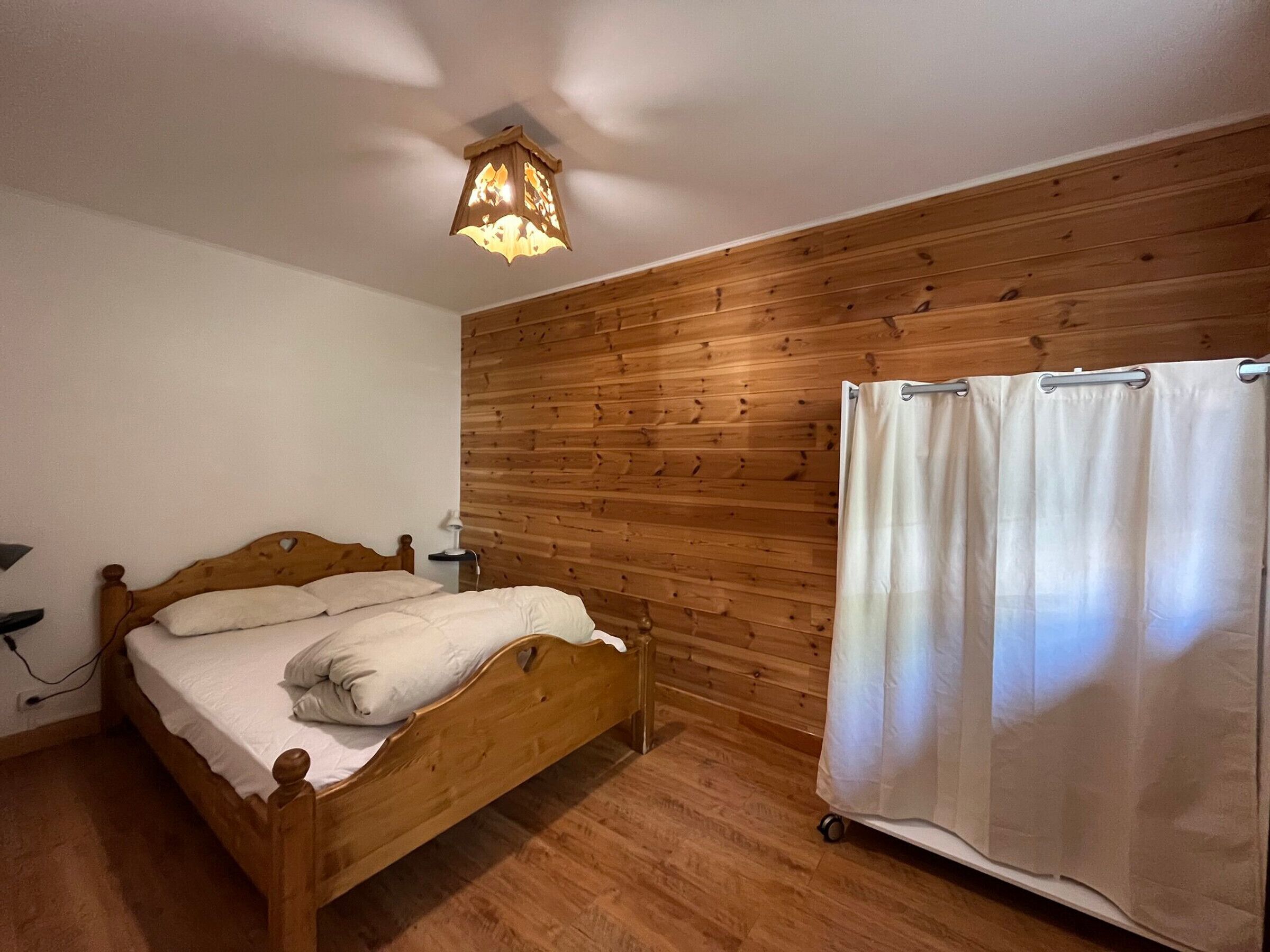 Ein Schlafzimmer mit einem hölzernen Bett, einem Nachttisch, einer Lampe und einem Vorhang.