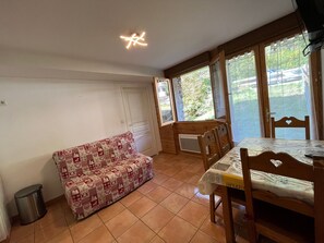 Un cuarto acogedor con una mesa de comedor de madera, un sofá estampado y amplias ventanas que ofrecen vistas al exterior.