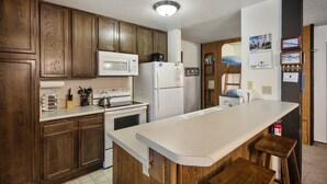 A kitchen with wooden cabinets, a white countertop, a microwave, a refrigerator, and a stove. - Crestview 29:  Walk to the Village, Near Blue Line (Mammoth Lakes)