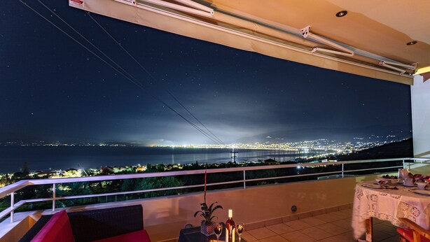 Een balkon met een eettafel, een bank en een uitzicht op een stadsbeeld in de nacht.