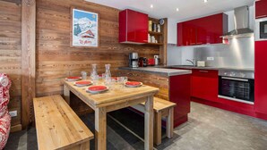 A modern kitchen with red cabinets, a wooden dining table, and a poster on the wall.
