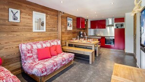 A cozy living area with a red and white patterned sofa, wooden walls, and a kitchen with red cabinets.
