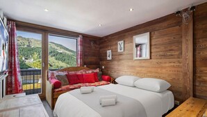 A bedroom with a large bed, a wooden wall, a window with a view of the countryside, and a small table.