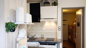 A compact kitchen with a dishwasher, a sink, and a microwave. There is a small plant on the countertop and a bag of laundry on the floor.