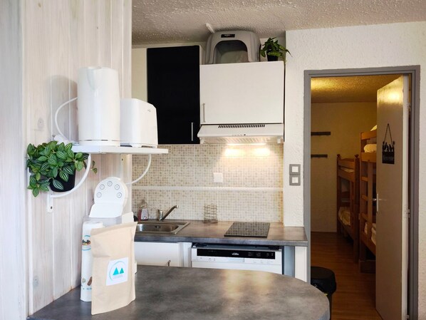 A compact kitchen with a dishwasher, a sink, and a microwave. There is a small plant on the countertop and a bag of laundry on the floor.