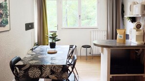 A dining area with a table, chairs, a potted plant, and a window with curtains.