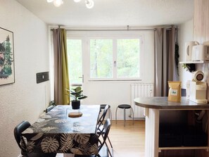 A dining area with a table, chairs, a potted plant, and a window with curtains.