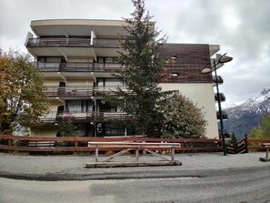 A multi-story building with balconies, a wooden fence, and a bench in front.