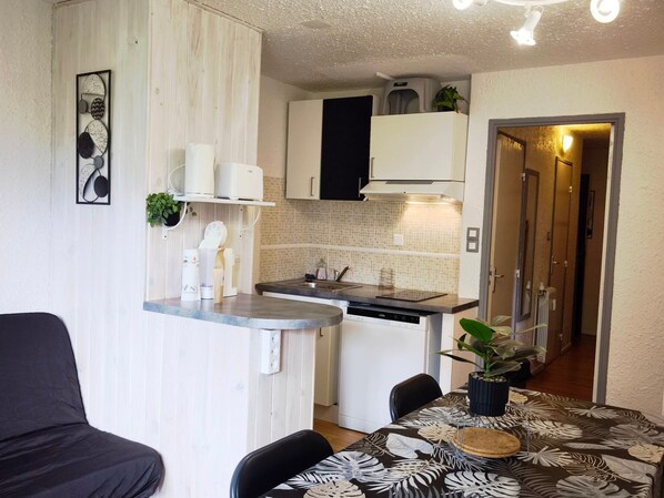 A compact kitchen with a built-in dishwasher, a small countertop, and a dining area with a table and chairs.