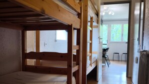 A bunk bed room with a wooden ceiling, a radiator, and a view of an outdoor area with chairs and a table.