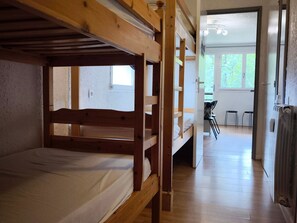 A bunk bed room with a wooden ceiling, a radiator, and a view of an outdoor area with chairs and a table.