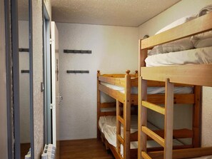 A narrow room with bunk beds, a door, and a wall-mounted shelf.