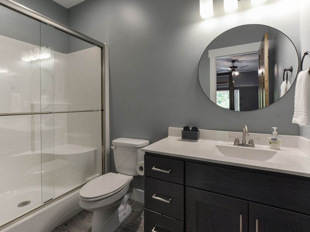 A modern bathroom with a glass shower enclosure, a toilet, a sink with a mirror, and dark cabinetry.