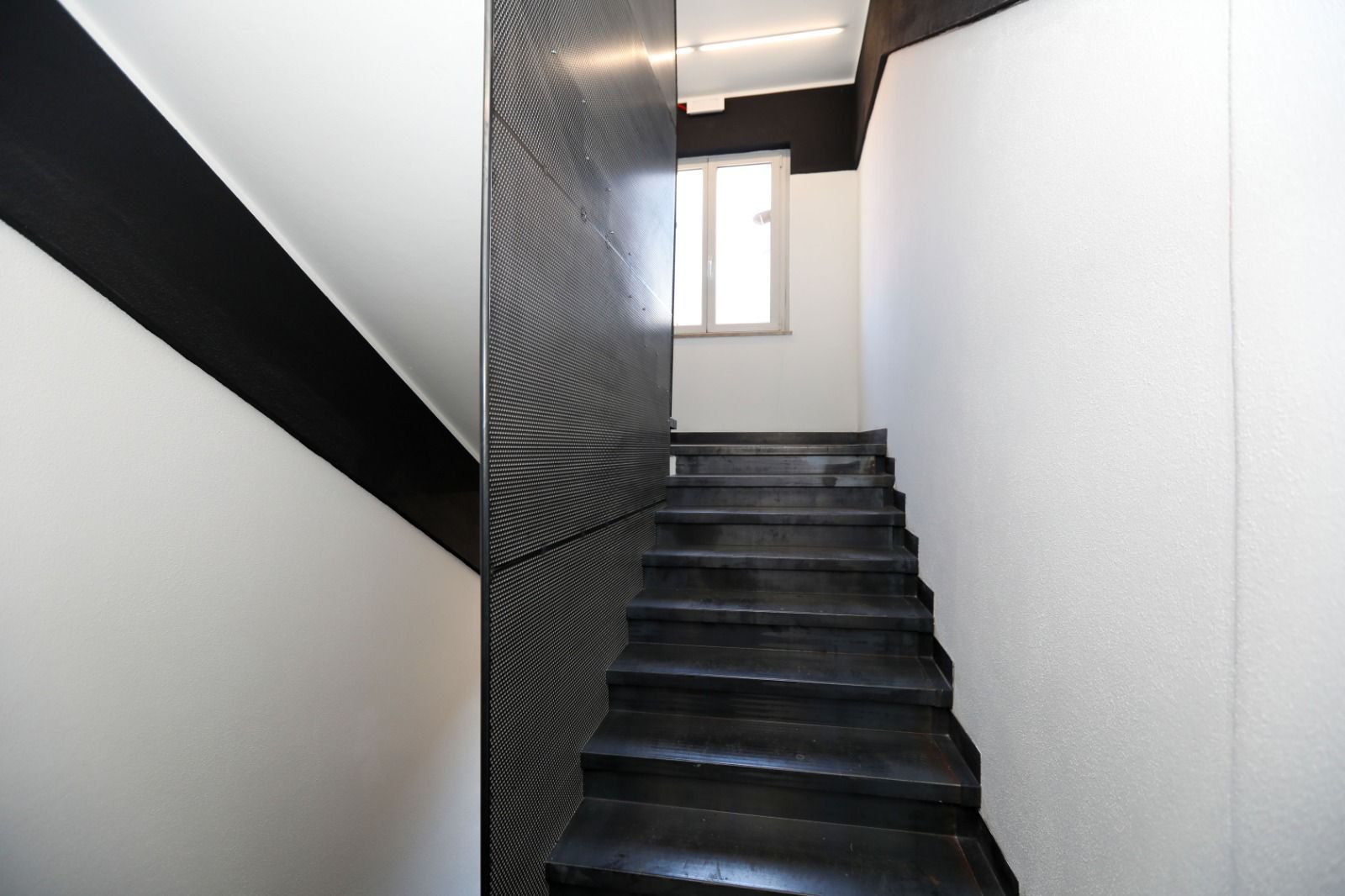 Un escalier moderne aux couleurs contrastées, en noir et blanc, menant à une pièce dotée d’une fenêtre.