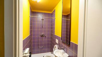 Une salle de bain avec des murs recouverts de carreaux violets, un plafond jaune, un lavabo blanc et des toilettes.