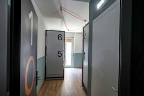 A hallway with numbered doors, a light fixture, and a view of a balcony. - Hotello (Trieste)