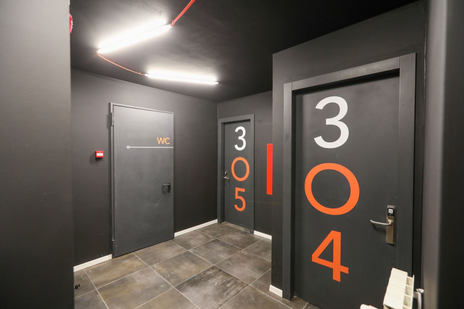 Ein Korridor mit Türen mit den Nummern 304 und 305, einem WC-Schild und einem roten Notausgangsschild.