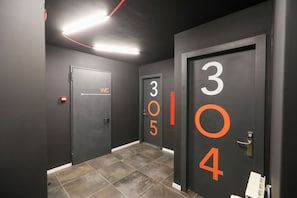 A corridor with doors numbered 304 and 305, a WC sign, and a red emergency exit sign. - Hotello (Trieste)