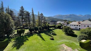 A well-maintained grassy area with neatly trimmed bushes and trees, surrounded by buildings with traditional architecture, set against a backdrop of mountains. - Quiet T2 apartment in Barcelonnette, city center (Barcelonnette)
