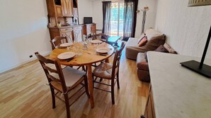 A dining area with a wooden table and chairs, a sofa, and a television in the background. - Quiet T2 apartment in Barcelonnette, city center (Barcelonnette)