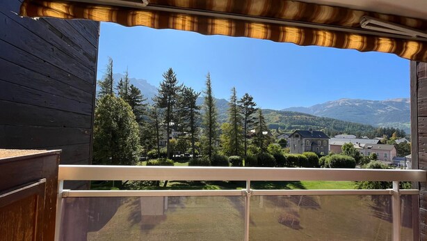 A balcony with a view of a mountainous landscape, a wooden structure, and a metal railing. - Quiet T2 apartment in Barcelonnette, city center (Barcelonnette)