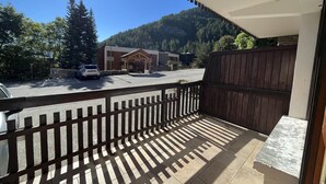 A balcony with a view of a parking area, a building with a wooden facade, and a mountainous backdrop.