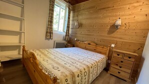 A wooden-paneled bedroom with a bed, a bedside table, a lamp, and a window with curtains. - Cozy chalet-style apartment in Pra-Loup, 4 guests (Pra-Loup)