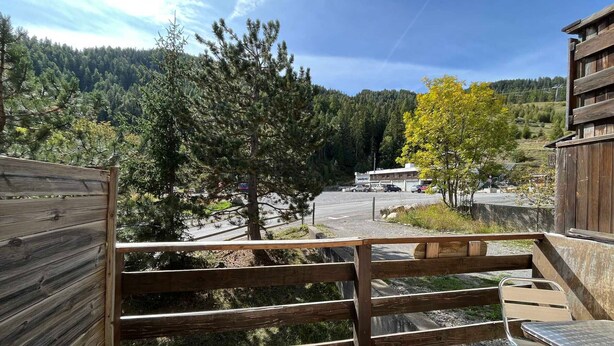 A wooden deck with a metal table and chairs, overlooking a parking area and a forested hillside. - Cozy chalet-style apartment in Pra-Loup, 4 guests (Pra-Loup)