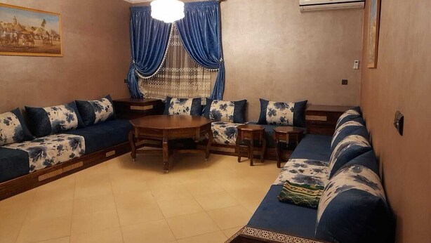 A living room with a sofa set, a wooden coffee table, and a chandelier. - Residence Annaser 3 Agadir (Hay Essalam,Agadir)