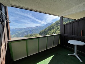 Un balcon avec vue sur les montagnes, une petite table et une moquette verte.