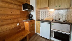 A compact kitchenette with wooden cabinetry, a microwave, a coffee maker, a small refrigerator, and a built-in oven. - Mountain Studio with Wifi 100m from Pra Loup 1600 Slopes (Pra-Loup)
