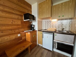 A compact kitchenette with wooden cabinetry, a microwave, a coffee maker, a small refrigerator, and a built-in oven. - Mountain Studio with Wifi 100m from Pra Loup 1600 Slopes (Pra-Loup)