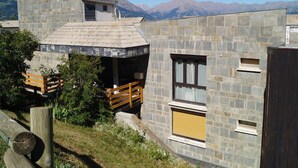 A stone building with a sloped roof, a wooden deck, and a window with a shutter. - Mountain Studio with Wifi 100m from Pra Loup 1600 Slopes (Pra-Loup)