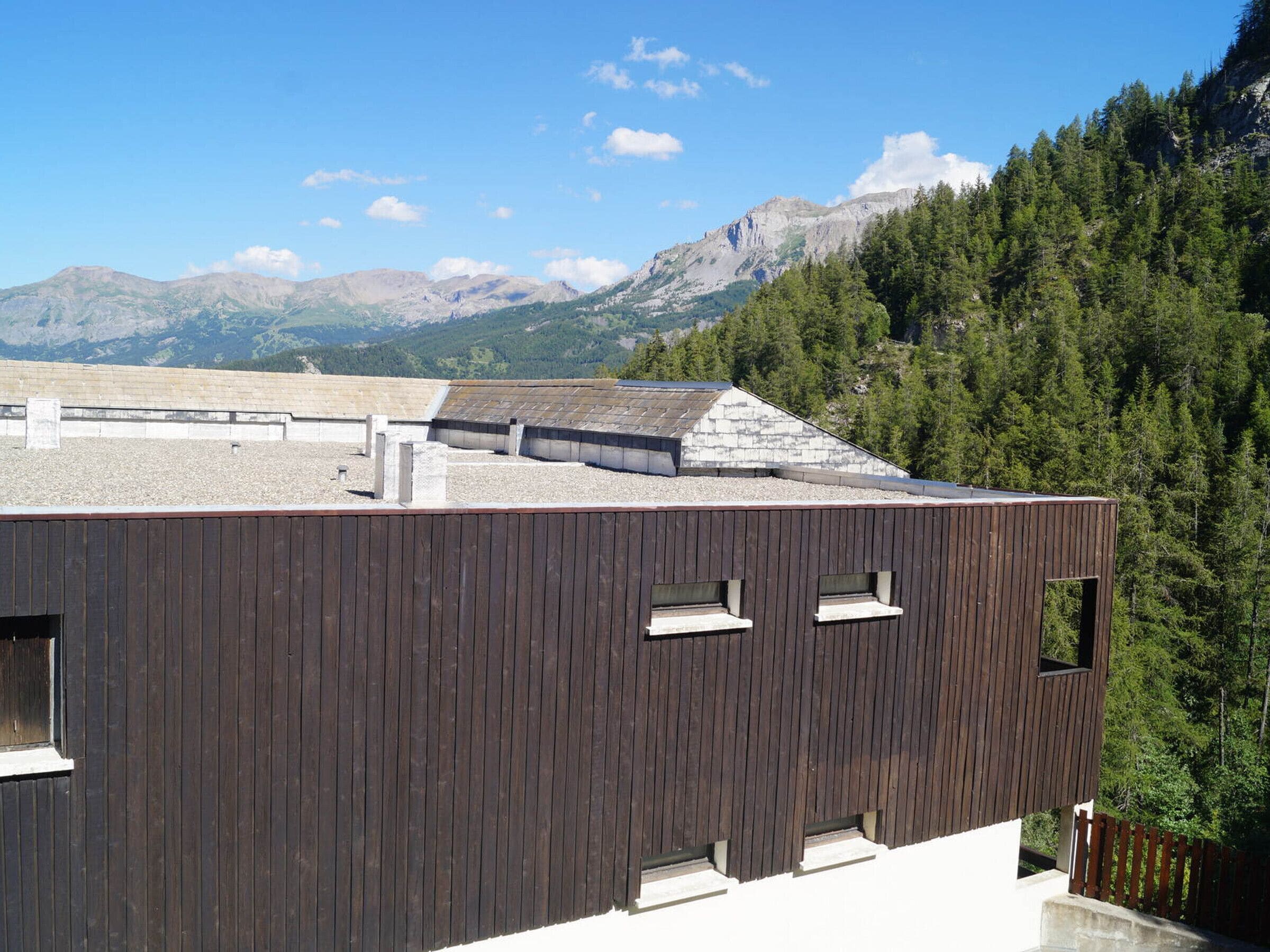 A modern building with a dark wooden exterior, multiple windows, and a sloped roof.