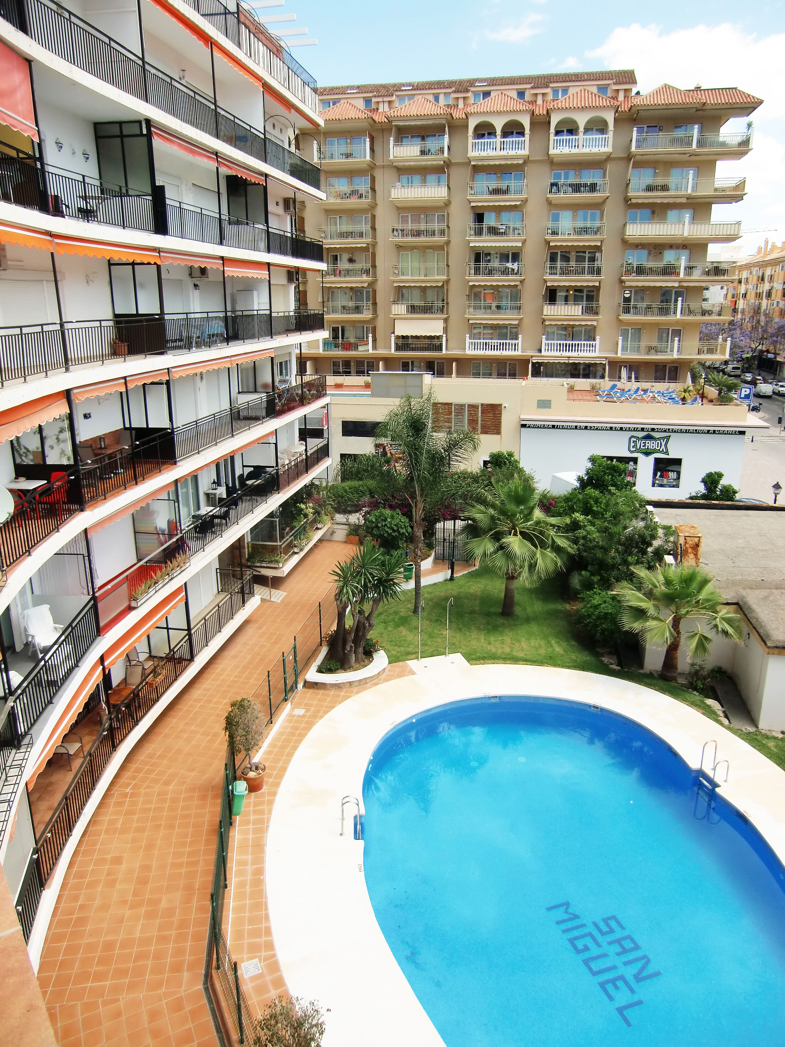 A multi-story hotel with a swimming pool, balconies, and a garden area.