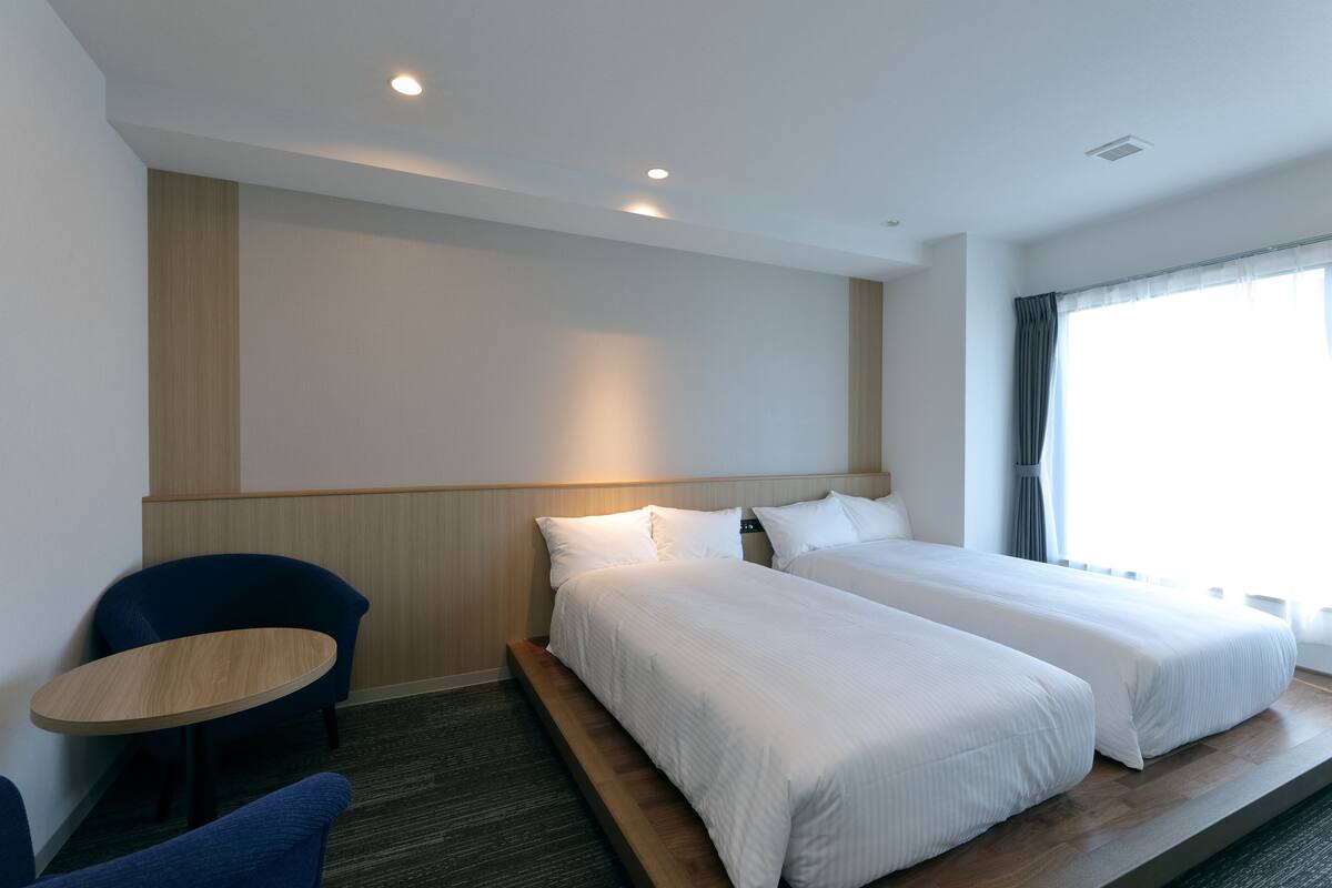 A hotel room with two beds, a small round table, and a chair.