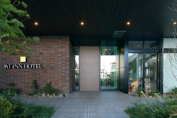 The entrance of the At Inn Hotel with a modern design, featuring a brick facade and a glass entrance. - At Inn Hotel Toyotashi station (Toyota)
