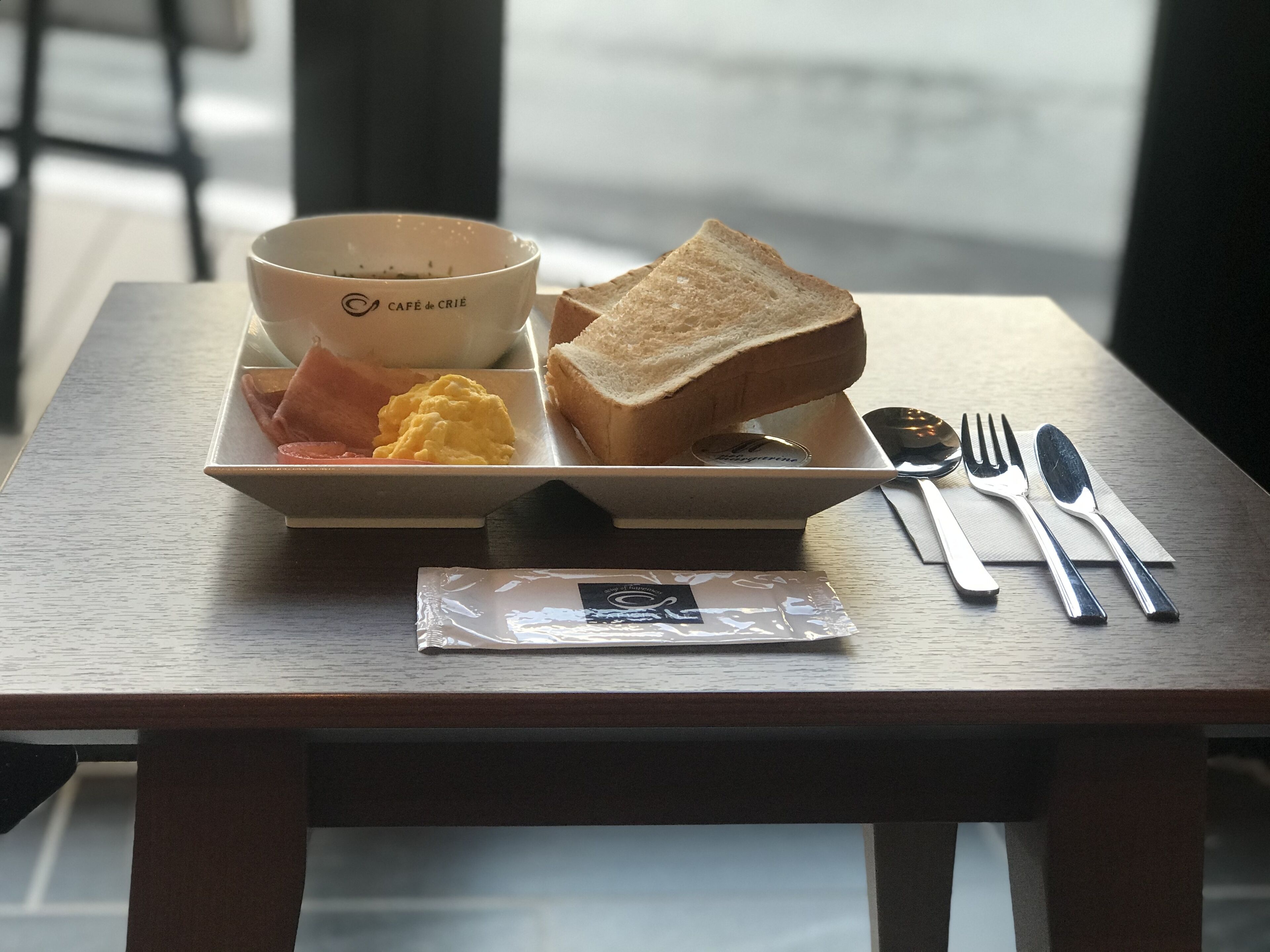 Una bandeja de desayuno con tostadas, huevos revueltos y jamón sobre una mesa de madera.