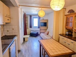 A compact kitchen with a dining table, a TV on a shelf, and a window with curtains.