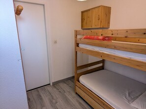 A bunk bed with a wooden headboard, a small cabinet above it, and a door with a round handle.