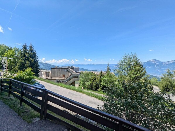 A modern building with a wooden facade, surrounded by greenery and a clear view of distant mountains.