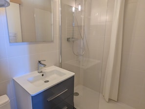 A modern bathroom with a white sink, a mirror, and a glass-enclosed shower.